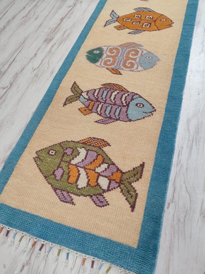 Handwoven beige fish runner rug by Oushakaura with colorful nautical fish pattern and teal borders