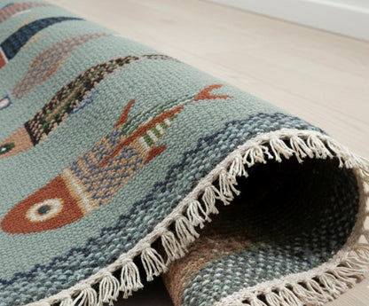 Folded handmade fish runner rug showing woven texture and artisan fringe detailing in soft blue green tones
