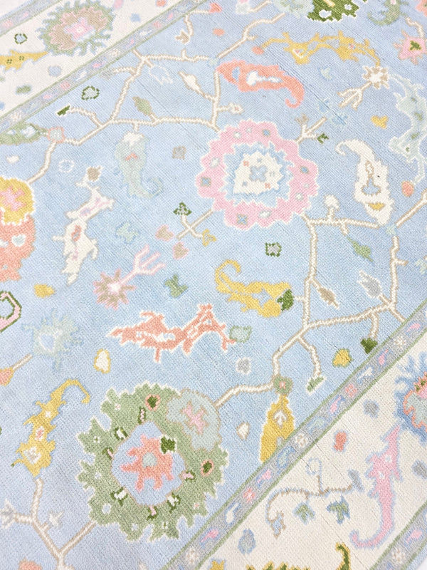 Close-up of pastel blue floral area rug with pink, green, yellow and ivory botanical details