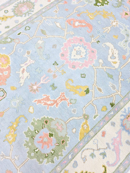 Close-up of pastel blue floral area rug with pink, green, yellow and ivory botanical details