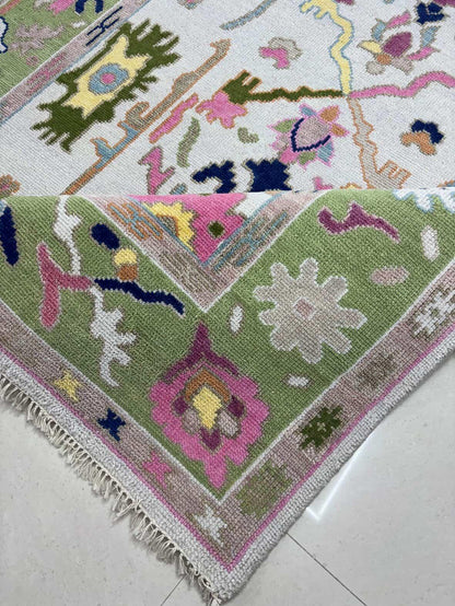 Close-up corner detail of handmade wool Oushak rug with pastel floral border and fringe edges