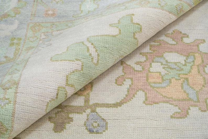 Textured surface of pastel ivory and green floral rug with traditional decorative motifs.