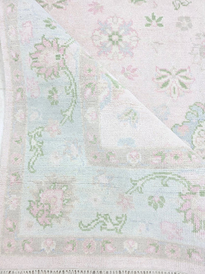Pink and blue vintage floral rug showing detailed border and pastel botanical motifs