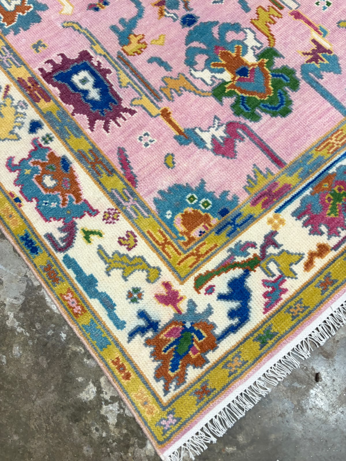Pink Oushak-inspired rug corner with colourful floral motifs and ivory decorative border