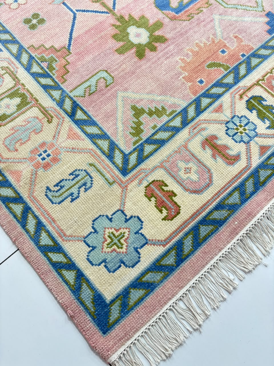 Close-up of blue geometric border on handmade blush pink Oushak rug.
