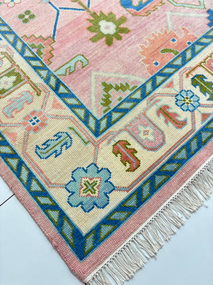 Close-up of blue geometric border on handmade blush pink Oushak rug.