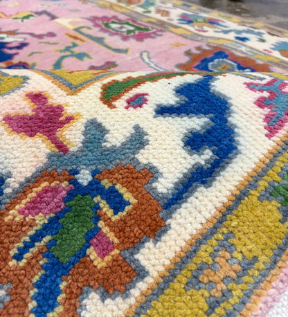 Close-up of colourful floral motifs and decorative patterns on a pink Oushak rug