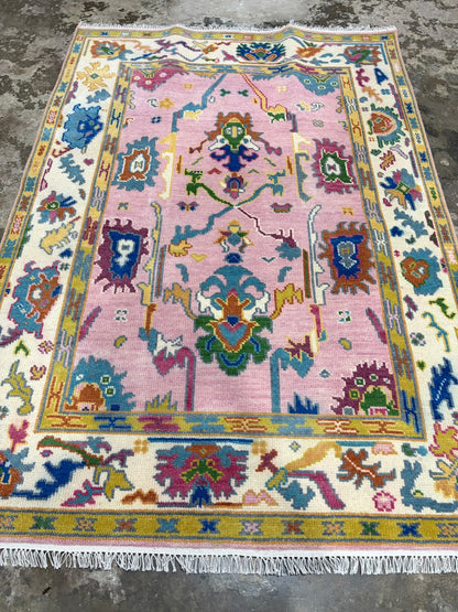 Full view of a pink hand-knotted wool Oushak rug with colourful traditional floral motifs