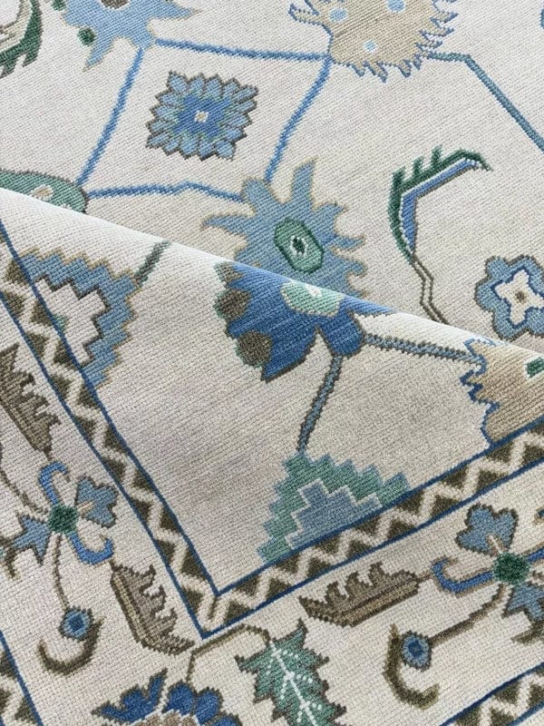 Folded corner of handmade wool Oushak style rug showing low pile, premium craftsmanship and floral border.