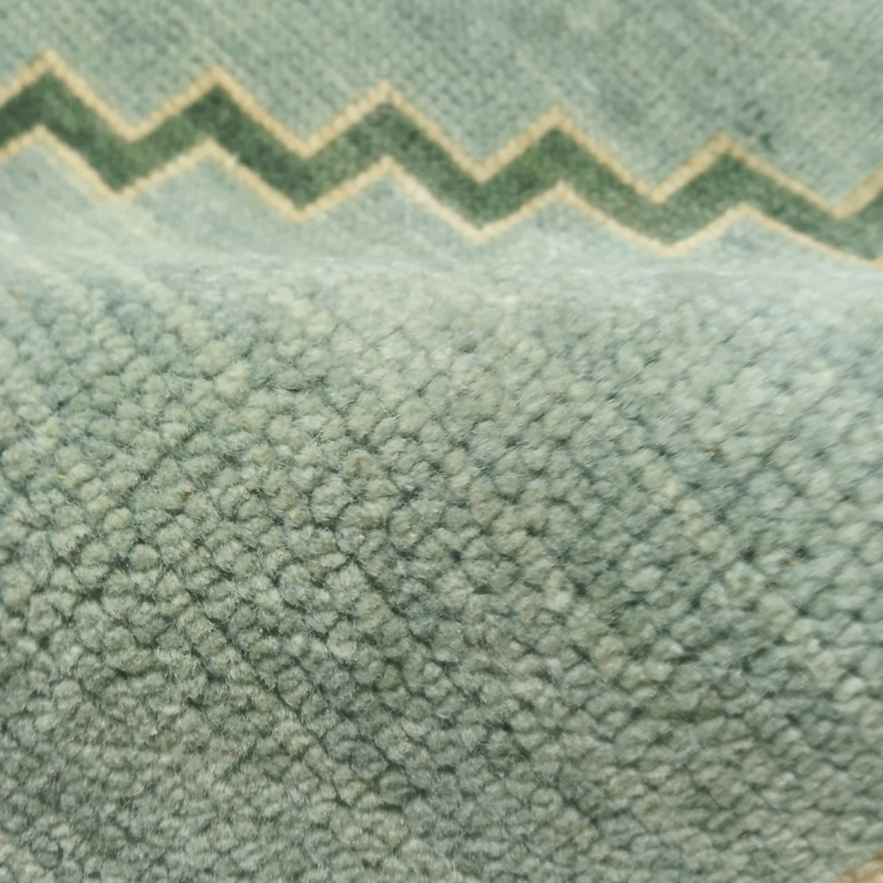 Angled view of minimalist sage green wool rug in full layout
