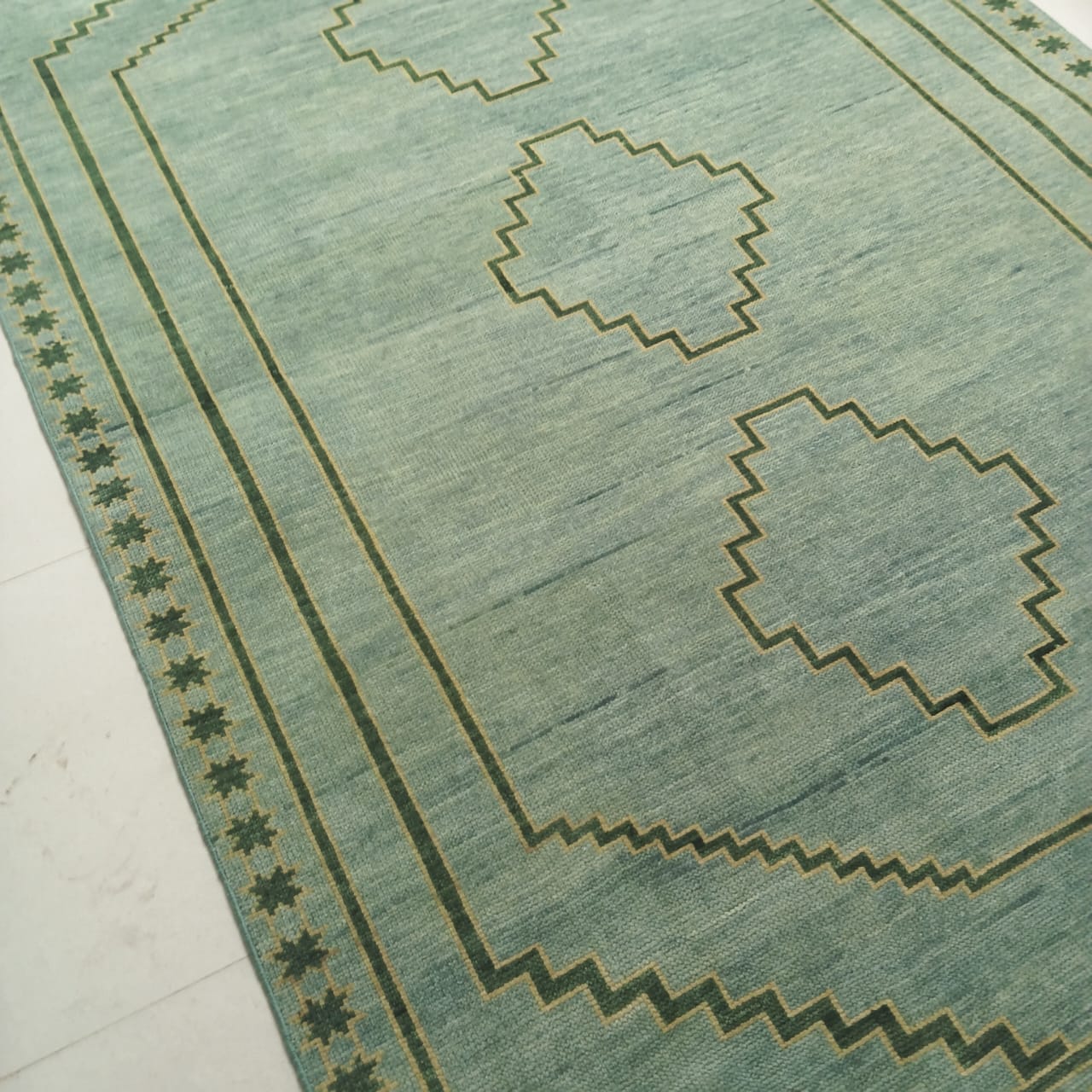 Geometric border detail on handmade sage green wool rug