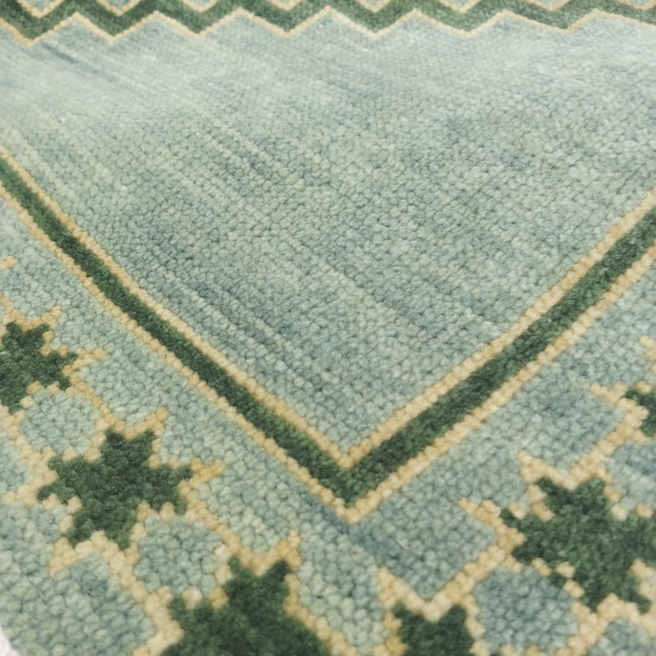 Close-up of sage green wool rug corner with handwoven texture