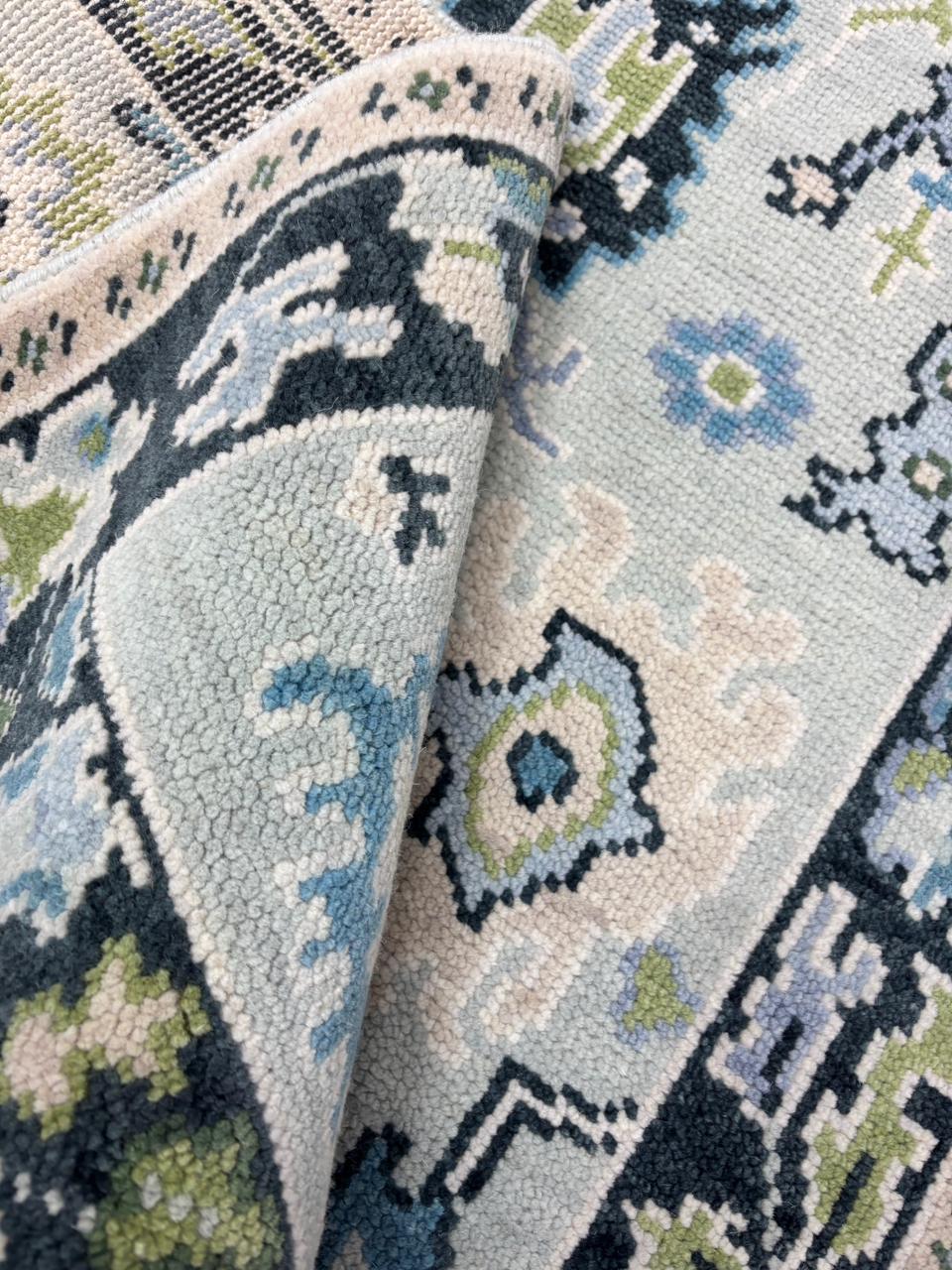 Corner detail of a handmade Scandinavian wool rug featuring a charcoal floral border and soft ice blue field.