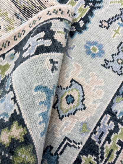 Corner detail of a handmade Scandinavian wool rug featuring a charcoal floral border and soft ice blue field.