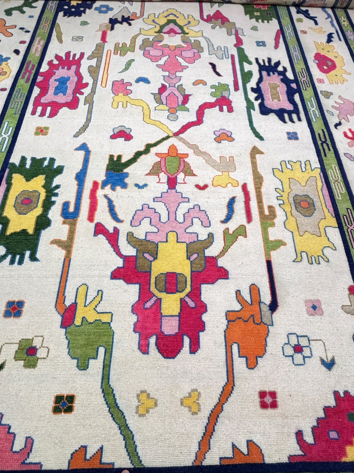 Full view of a handmade Nordic folk art wool rug with colorful abstract motifs and decorative green border.