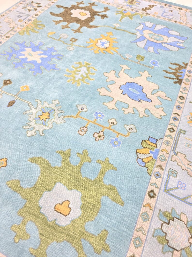 Angled view of sky blue Oushak rug showing colorful floral medallion pattern