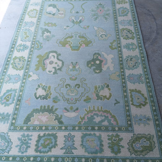 Handwoven sky blue and sage green Oushak wool rug with traditional Turkish floral border design