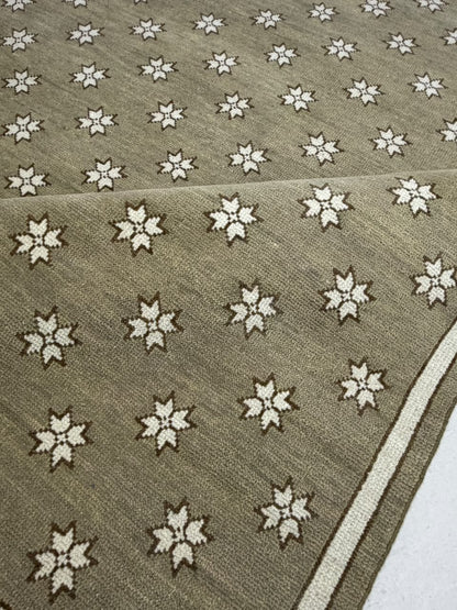 Folded corner of a taupe star-patterned rug showing the border and reverse side.