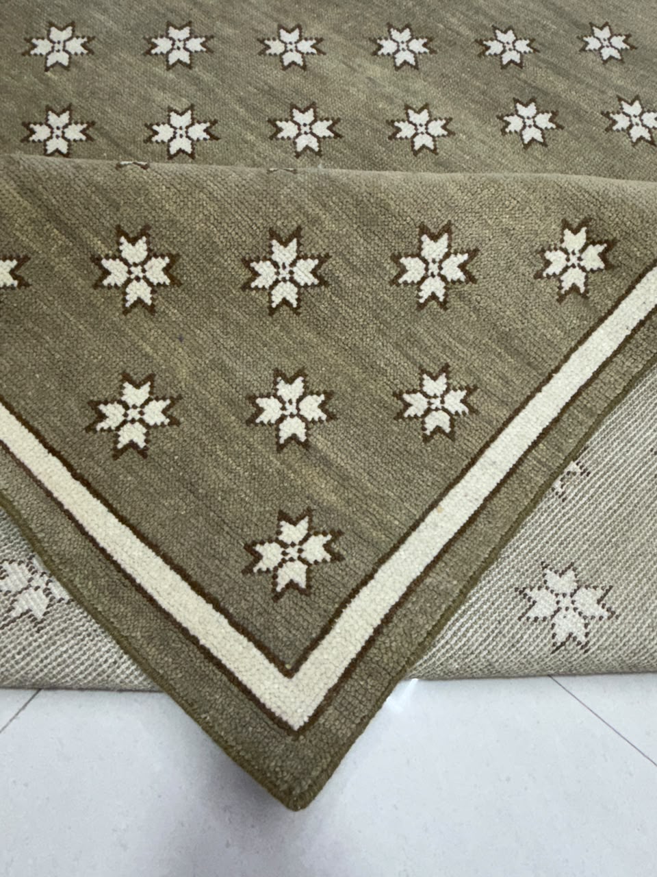Folded corner of taupe star pattern rug showing the border and reverse side.