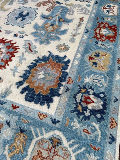 Corner detail of handmade Oushak rug with decorative floral border and ivory field