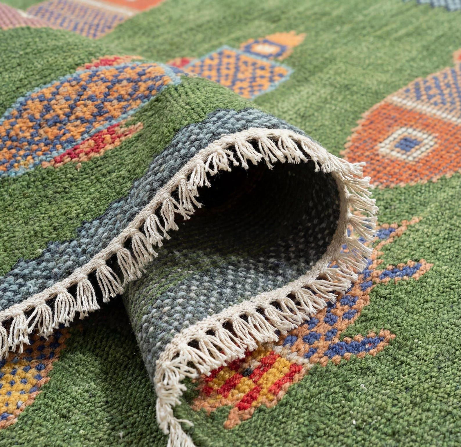 Folded handmade wool fish rug showing fringe edges and artisan woven backing